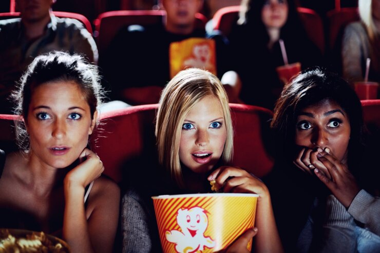 Wow popcorn and women in the cinema watching a movie for entertainment while eating a snack Face expression and food with shocked young friends in a theater audience to experience a film together